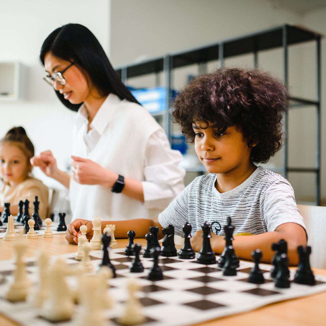 Children involved in gameschooling playing chess with teacher in background